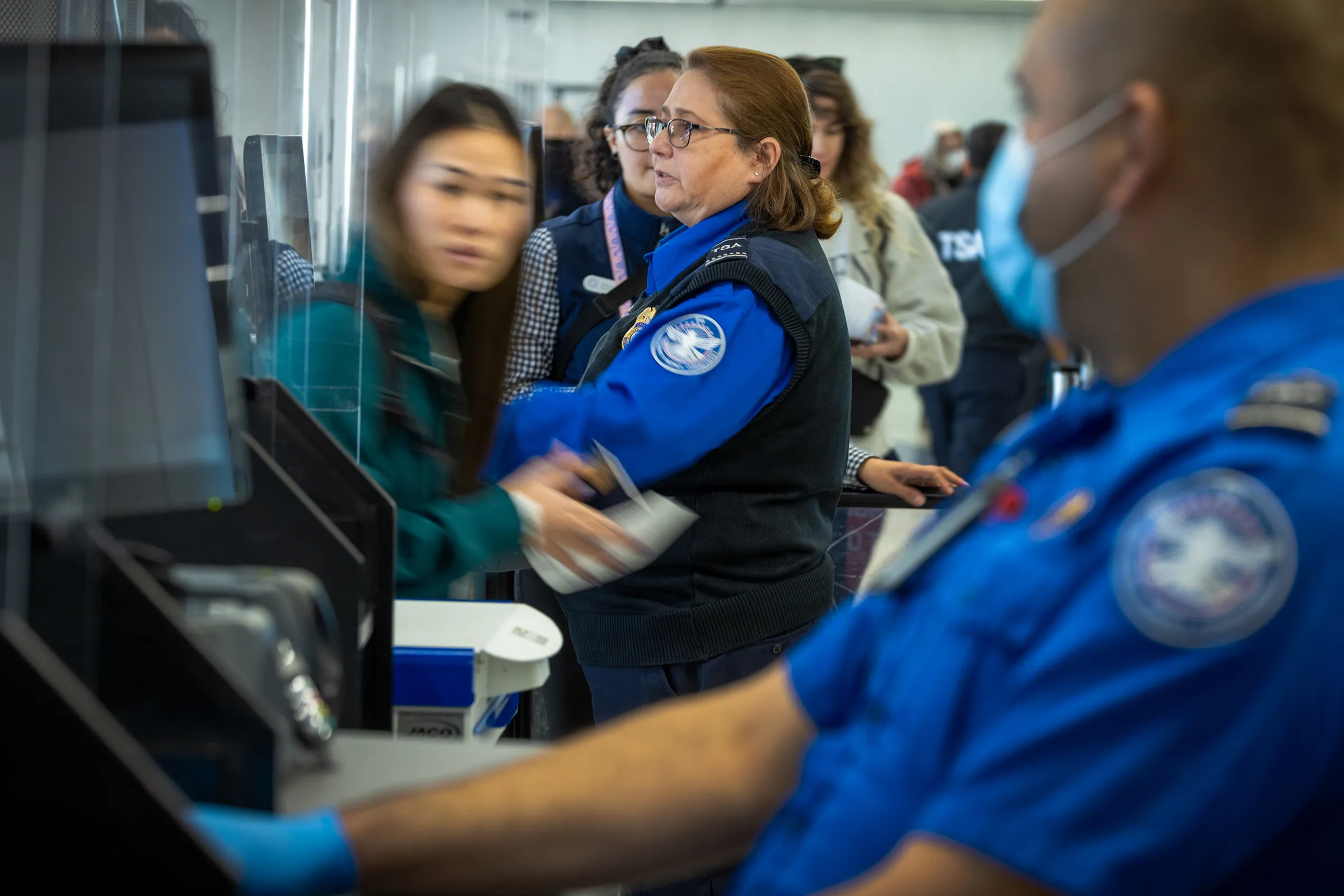 TSA officers in blue uniforms conducting passenger screenings at a busy airport security checkpoint, illustrating E.K. Associates' expertise in transportation safety and aviation security operations.