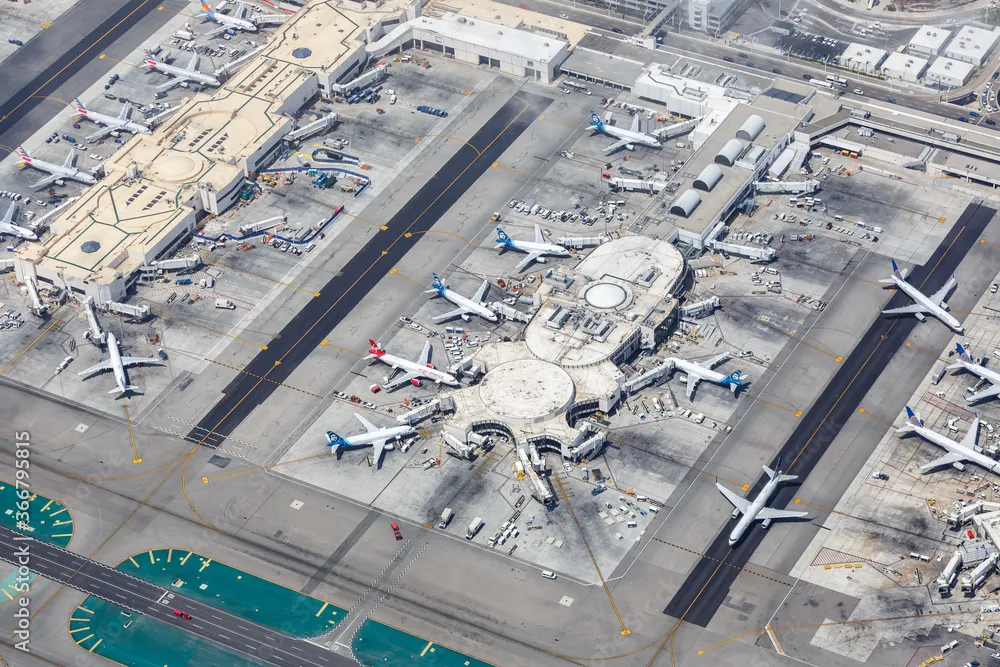 An aerial birds-eye view of a busy airport terminal hub with multiple airplanes docked at gates, ground service equipment, and taxiway markings.