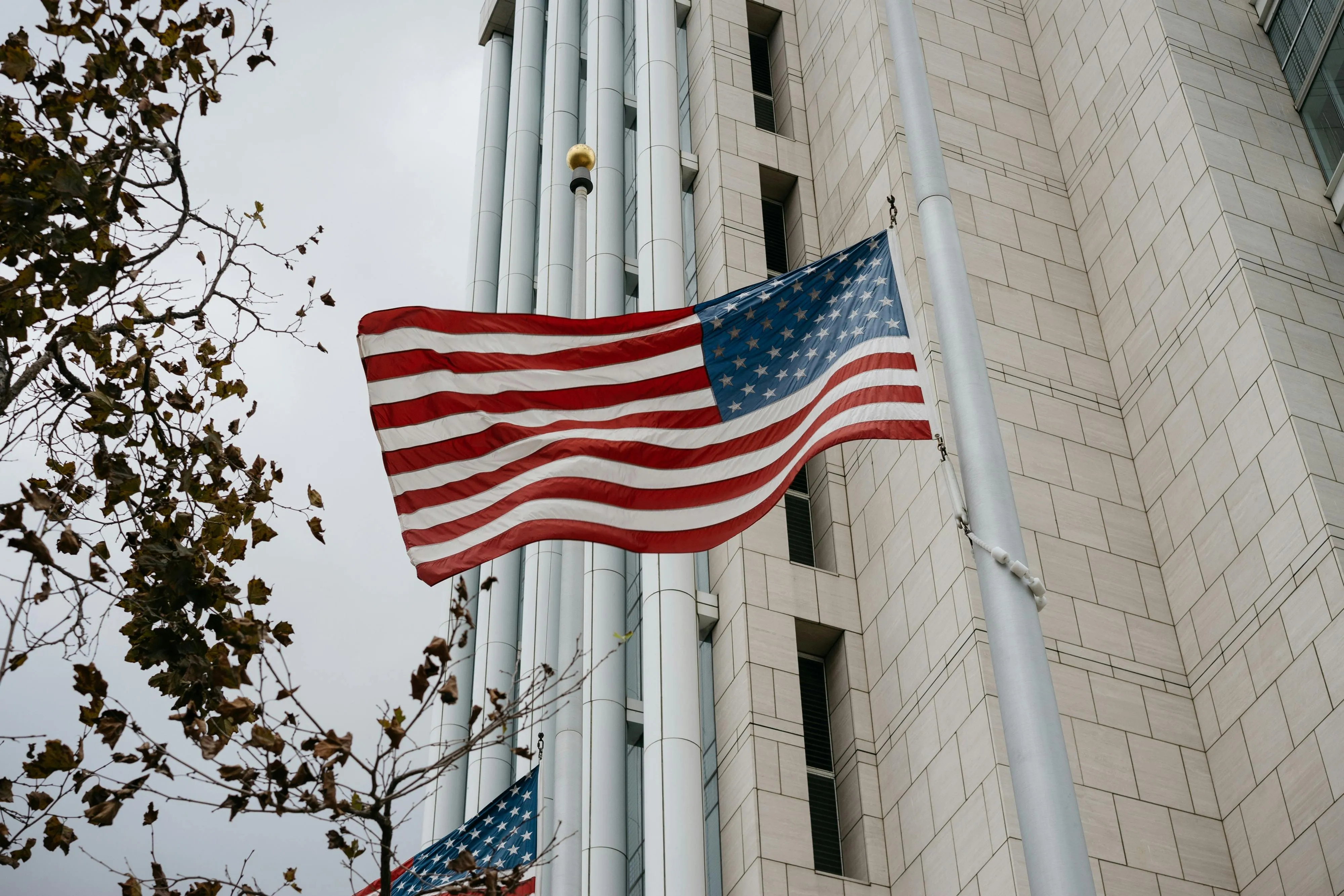 The United States flag waving in front of the modern stone and glass facade of a government office building, representing E.K. Associates' dedication to public sector projects.