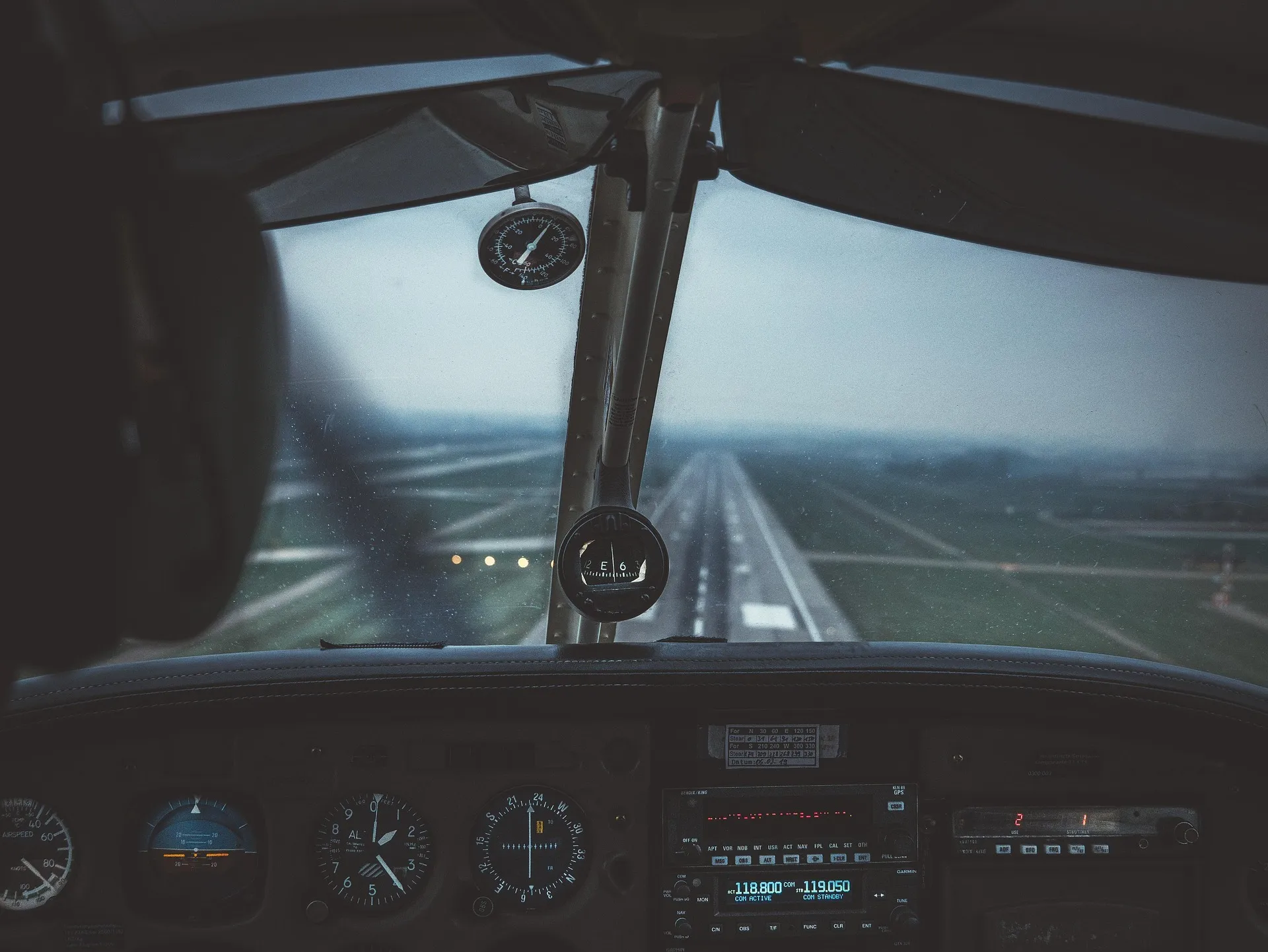 A pilot's-eye view from inside an aircraft cockpit, looking out over the runway during an approach, with illuminated instrument panels and navigation gauges in the foreground.