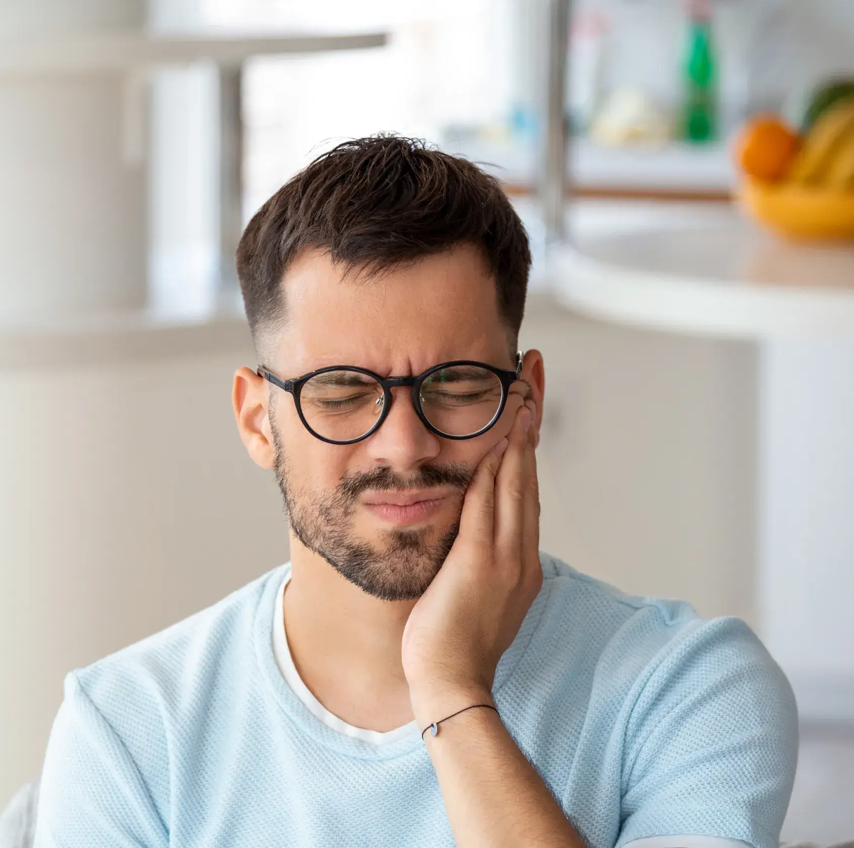 Man with glasses holding his cheek in pain, indicating a toothache.