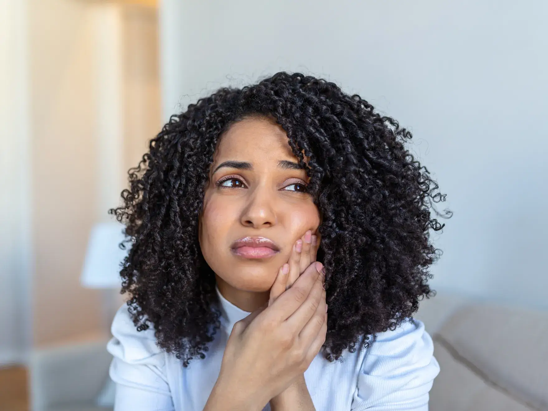 Woman with curly hair holding her cheek in pain, indicating a toothache.