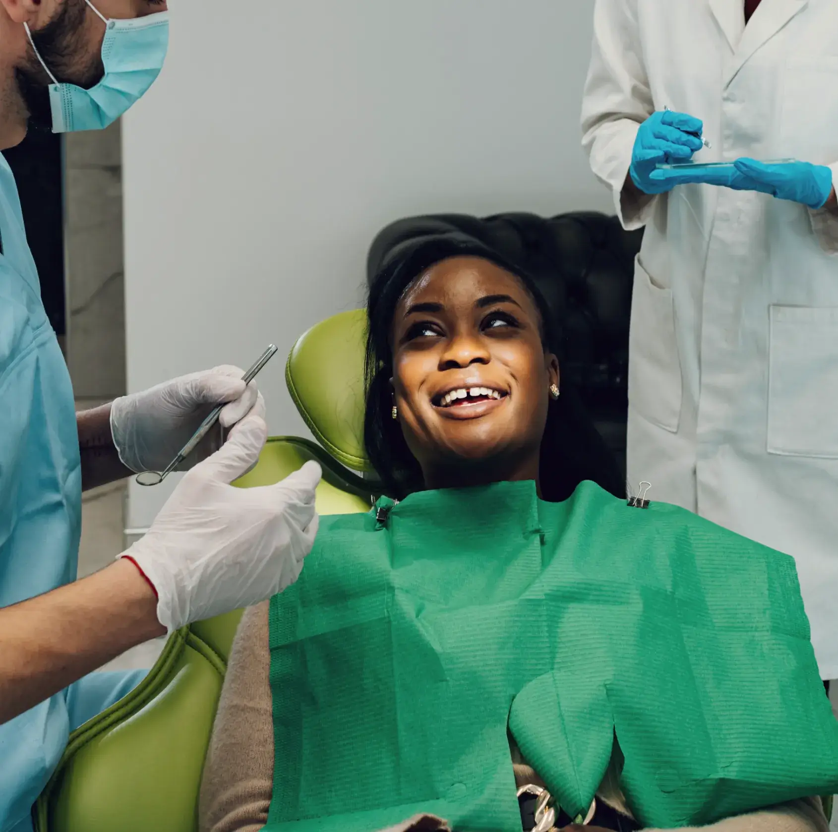 Smiling woman sitting in dental chair with green bib, interacting with dentist wearing gloves and mask.