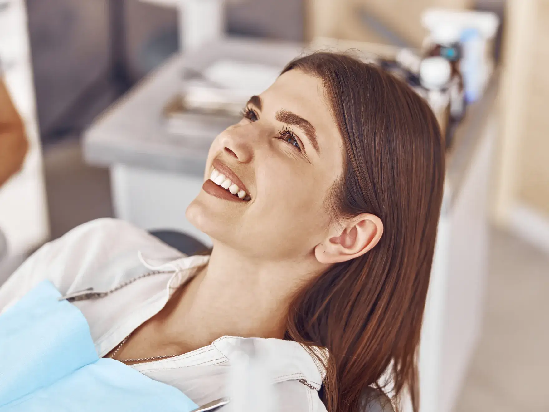 Smiling woman reclining in a dental chair wearing a blue dental bib.