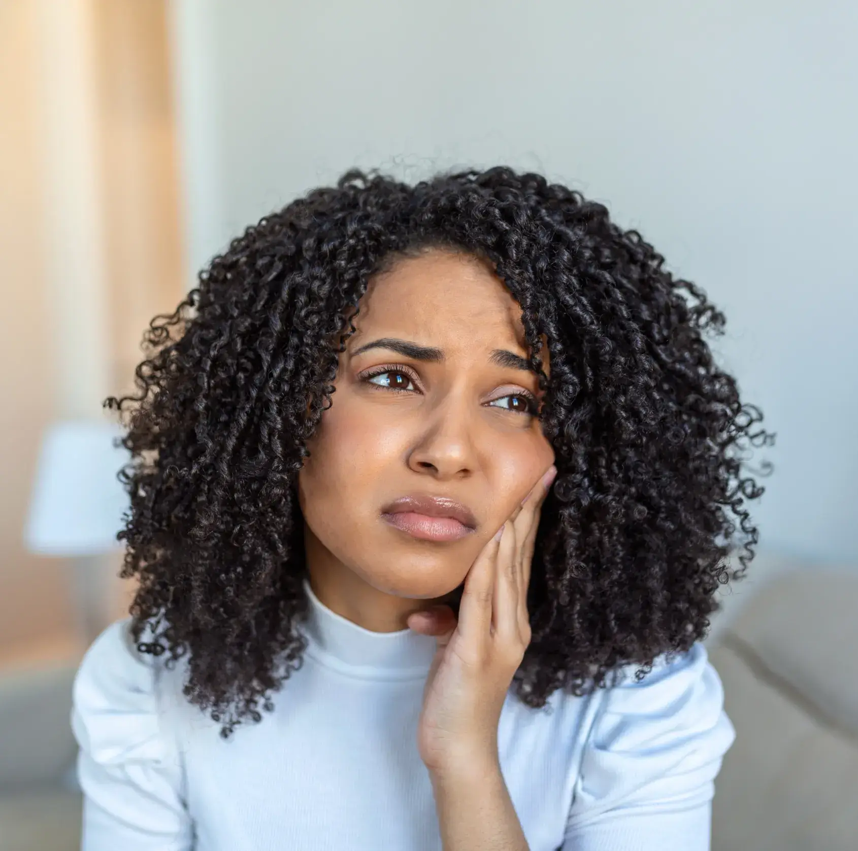 Young woman with curly hair holding her cheek in pain, expressing toothache or dental discomfort.