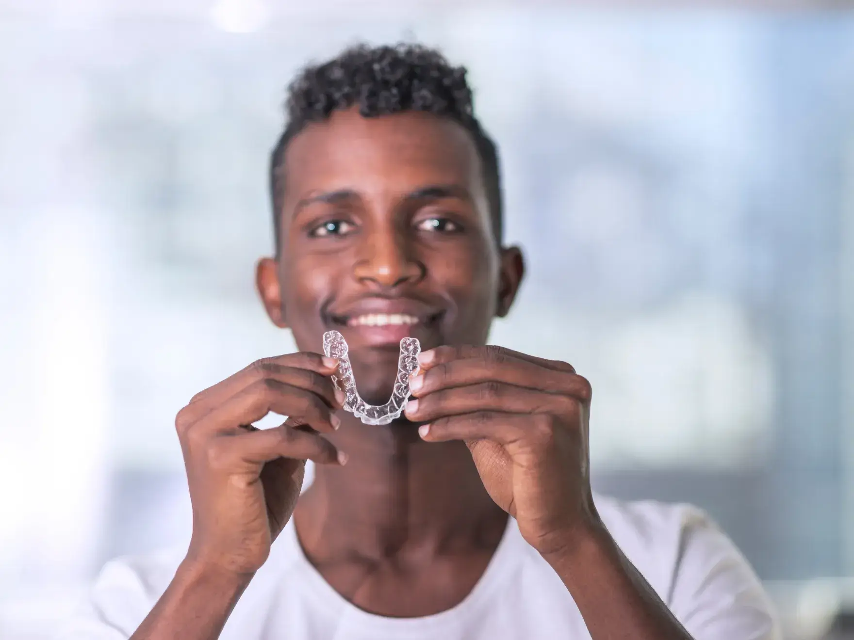 Smiling man holding clear dental aligners with both hands in front of his face.