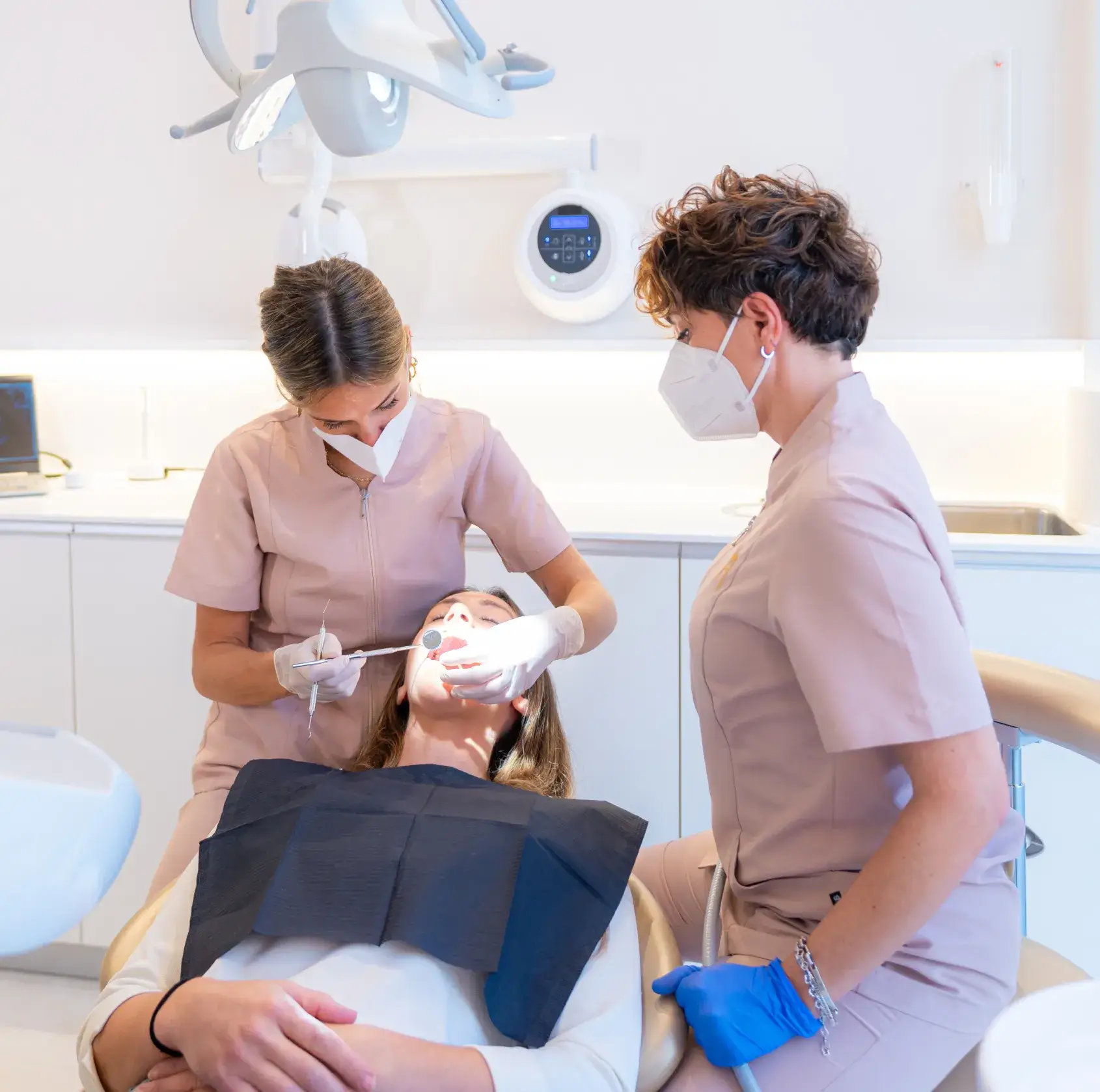 Dentist and assistant wearing masks performing dental cleaning on a patient reclining in a dental chair.