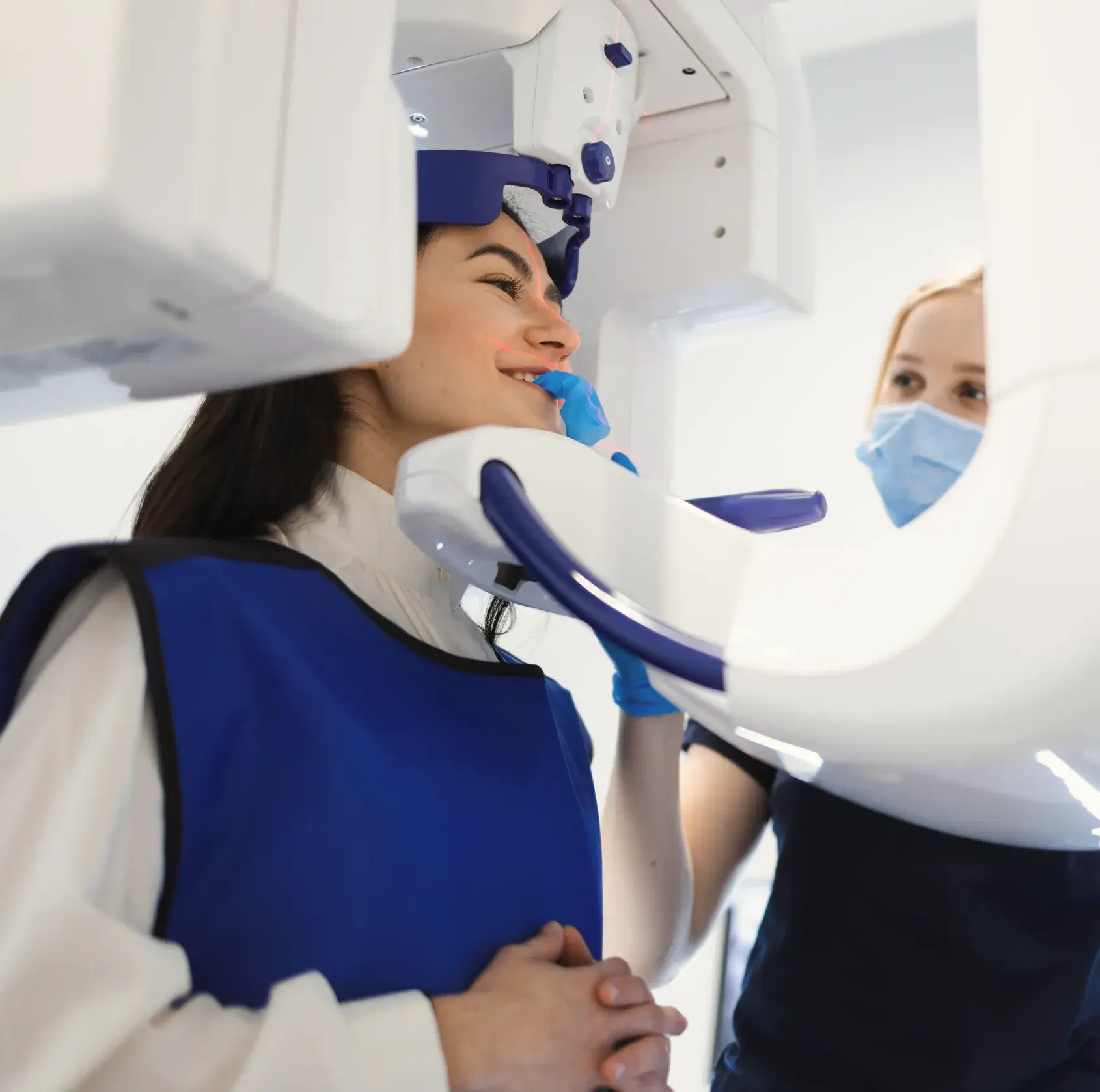 Woman wearing blue protective vest having a dental X-ray with a technician adjusting the machine.