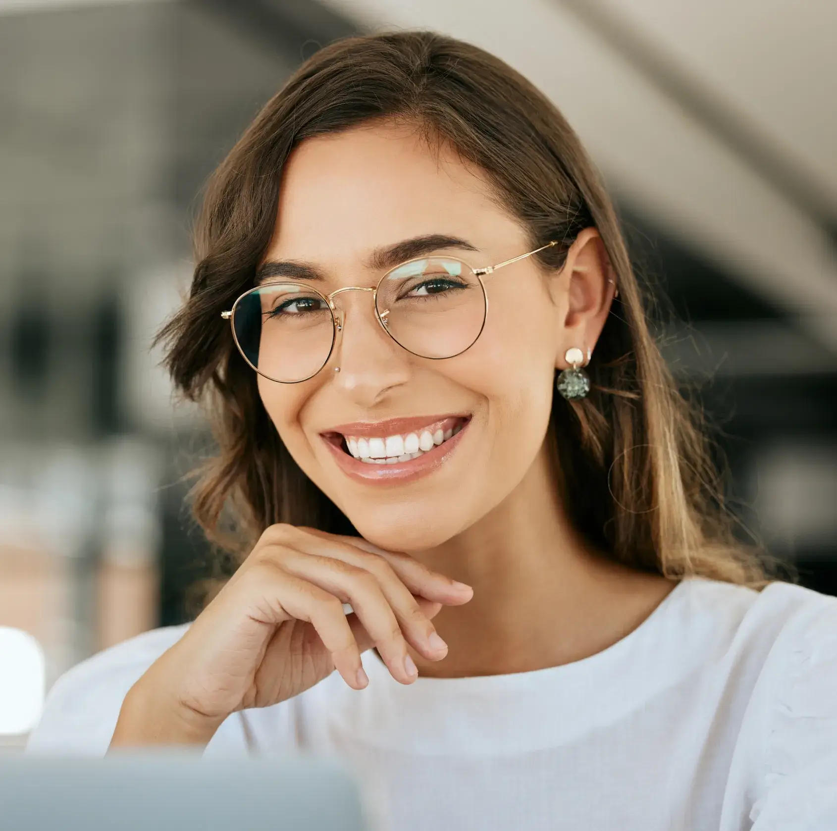 Smiling woman wearing round glasses and pearl earrings, resting her chin on her hand.