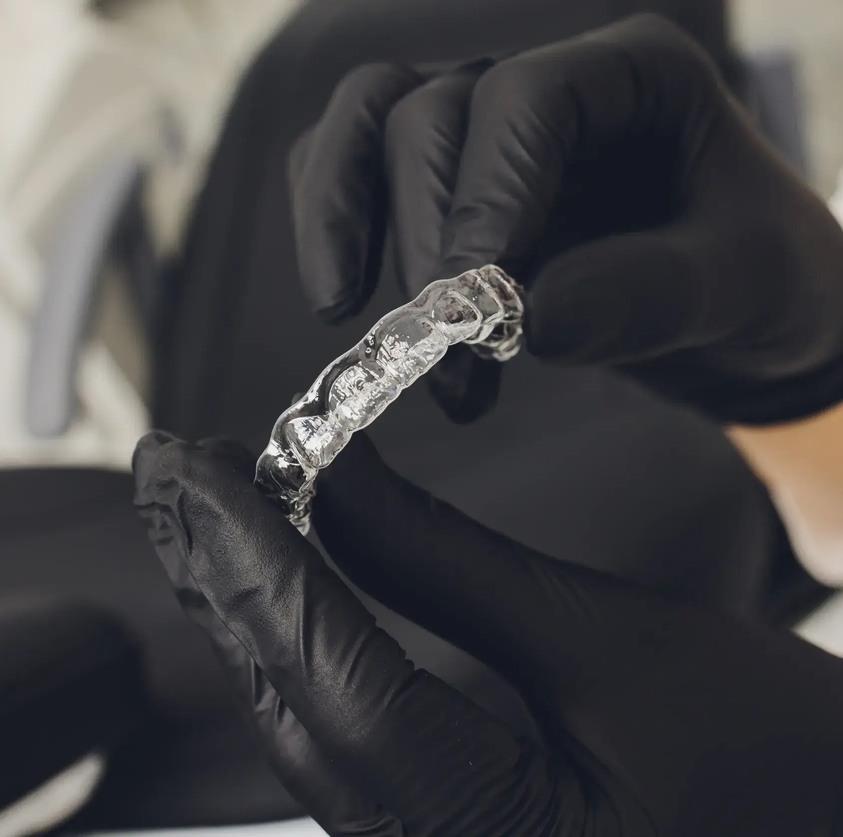 Hands in black gloves holding a clear dental aligner.