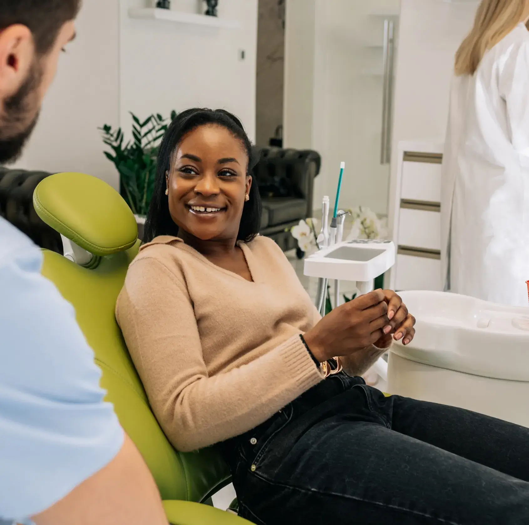 Smiling woman sitting in a green dental chair talking to a dentist in a clinic.