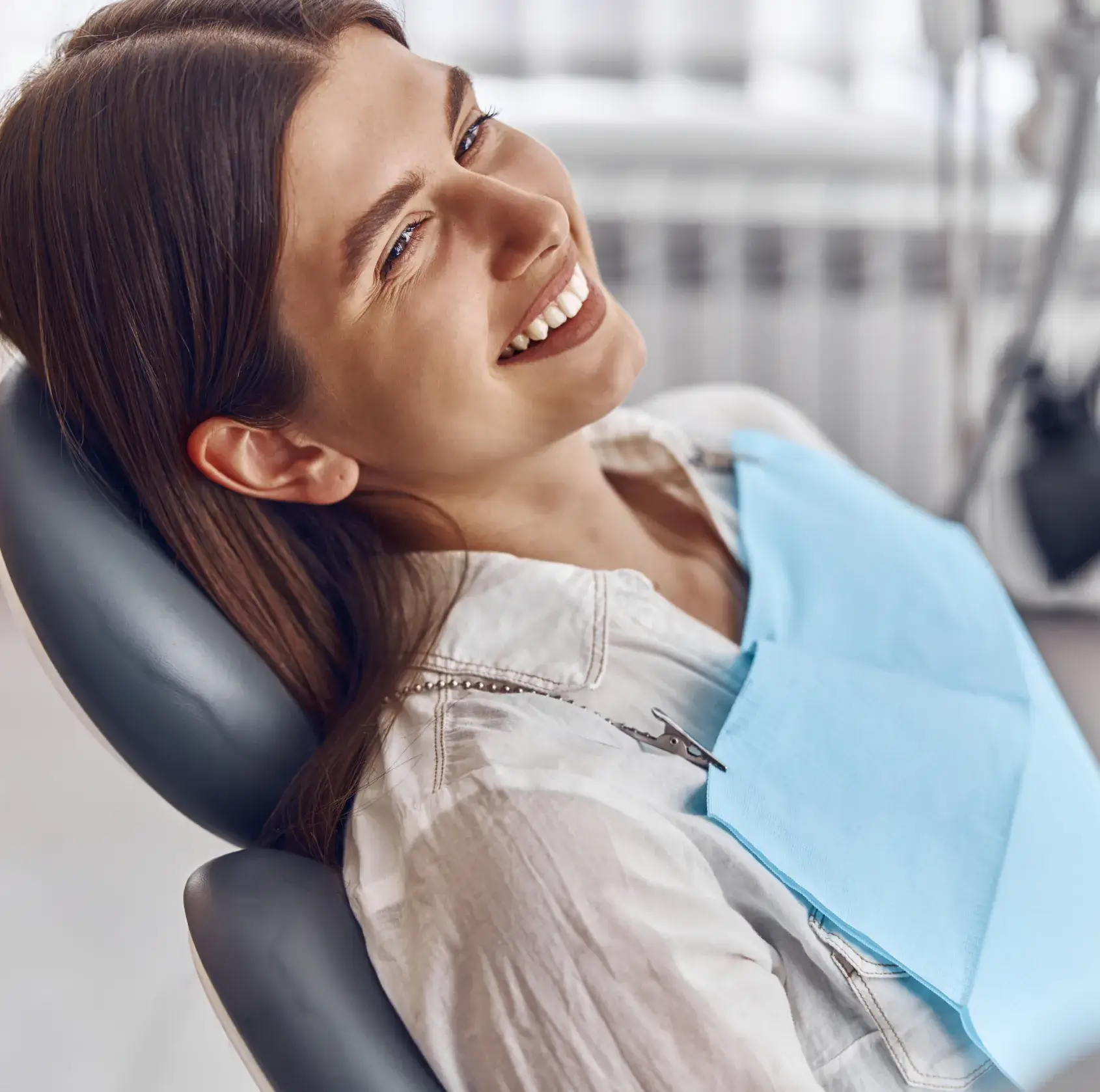 Smiling woman reclining in a dental chair wearing a blue dental bib.