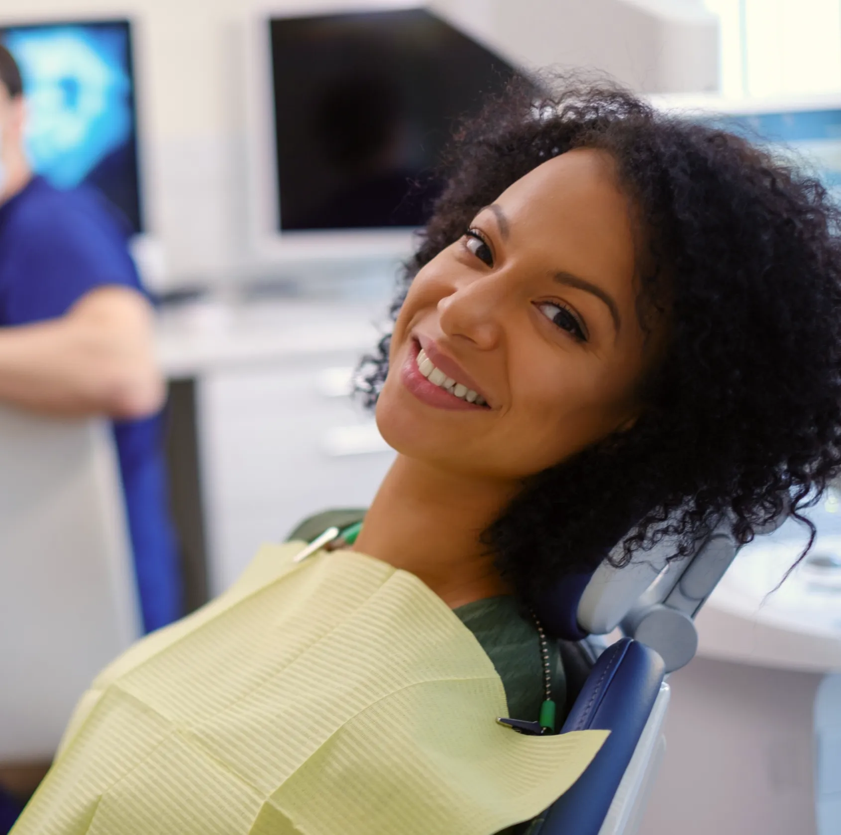 Smiling woman reclining in a dental chair wearing a protective bib in a dental office.