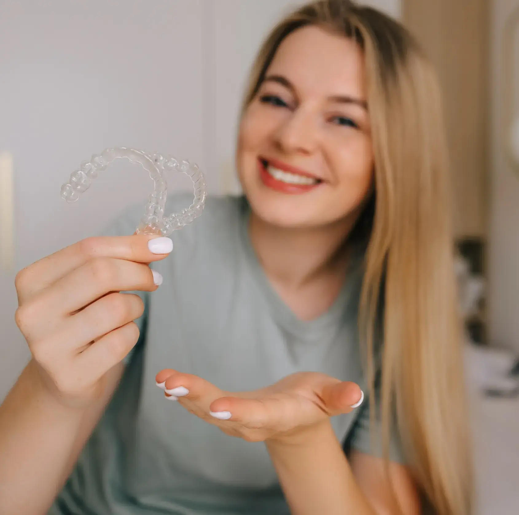 Smiling woman holding two clear Invisalign aligners in one hand and gesturing with the other.