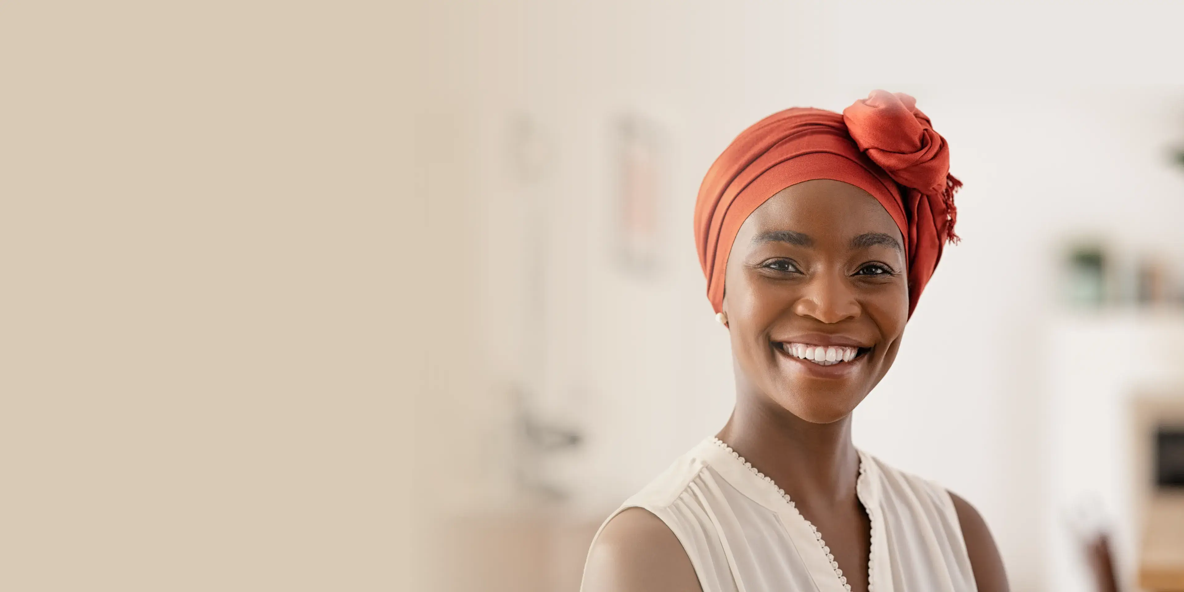 Smiling woman with a red headwrap and white blouse in a softly lit indoor setting.