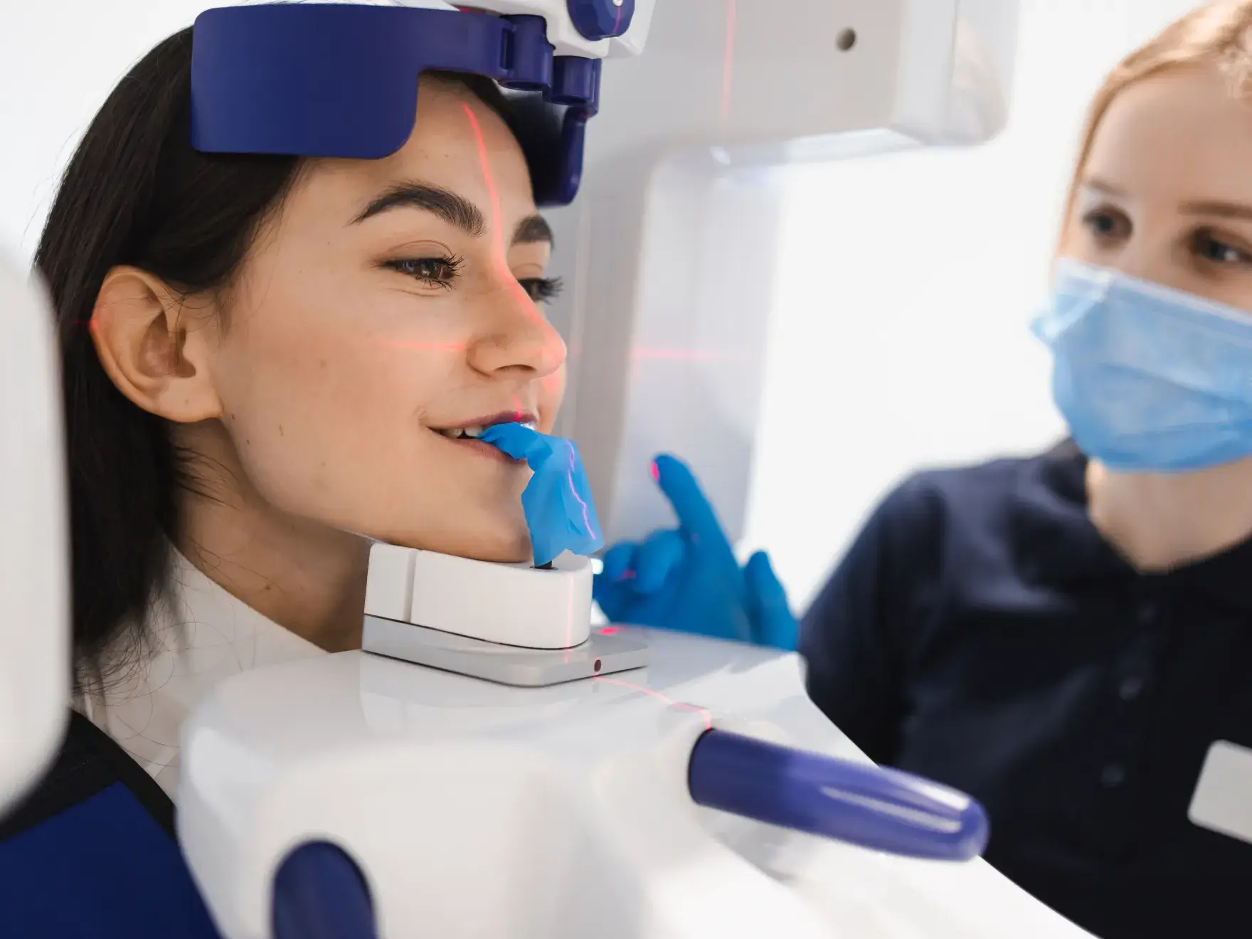 Patient undergoing dental 3D imaging with a technician guiding the procedure wearing a mask and gloves.