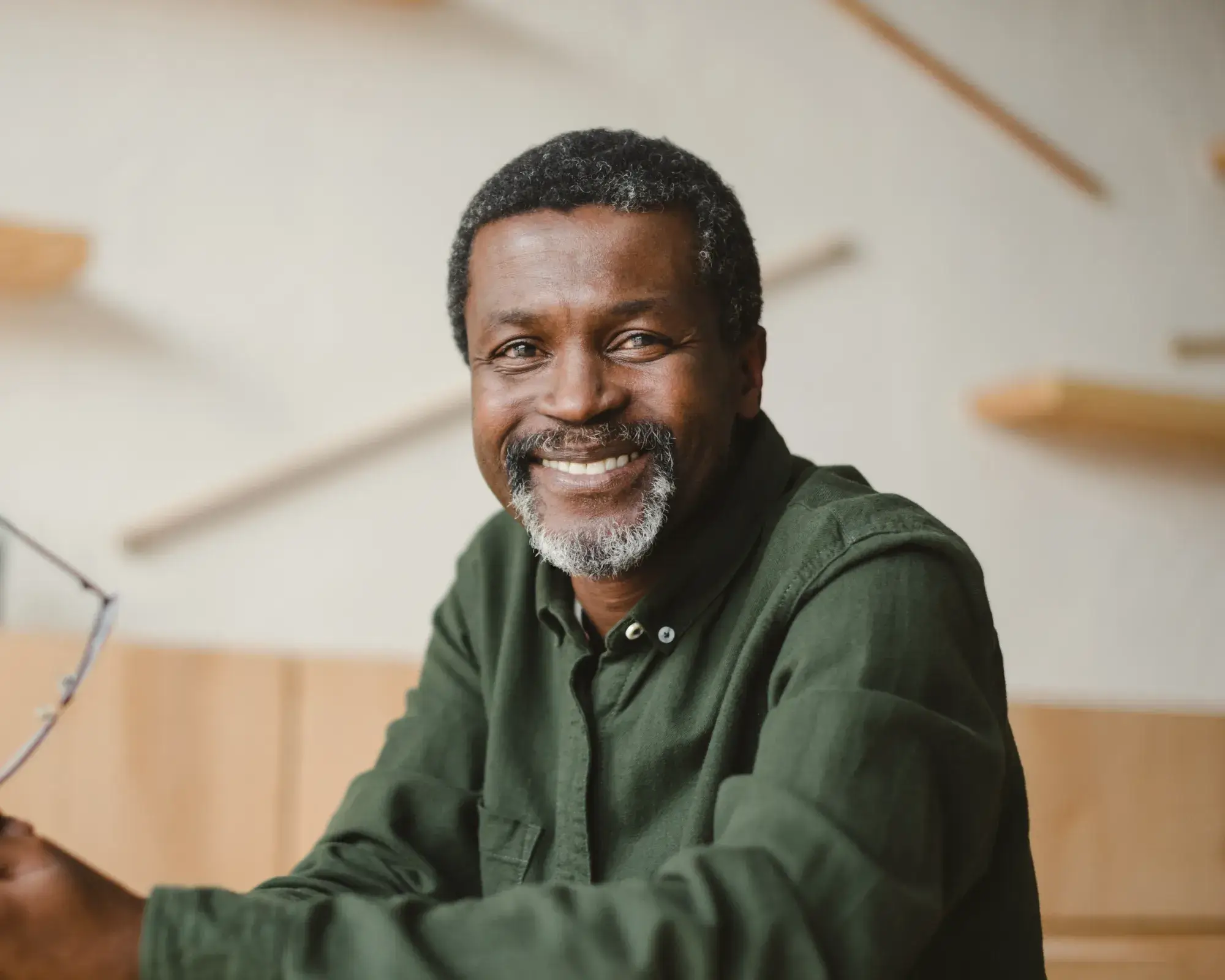 Smiling middle-aged man with salt-and-pepper beard wearing a green shirt indoors.