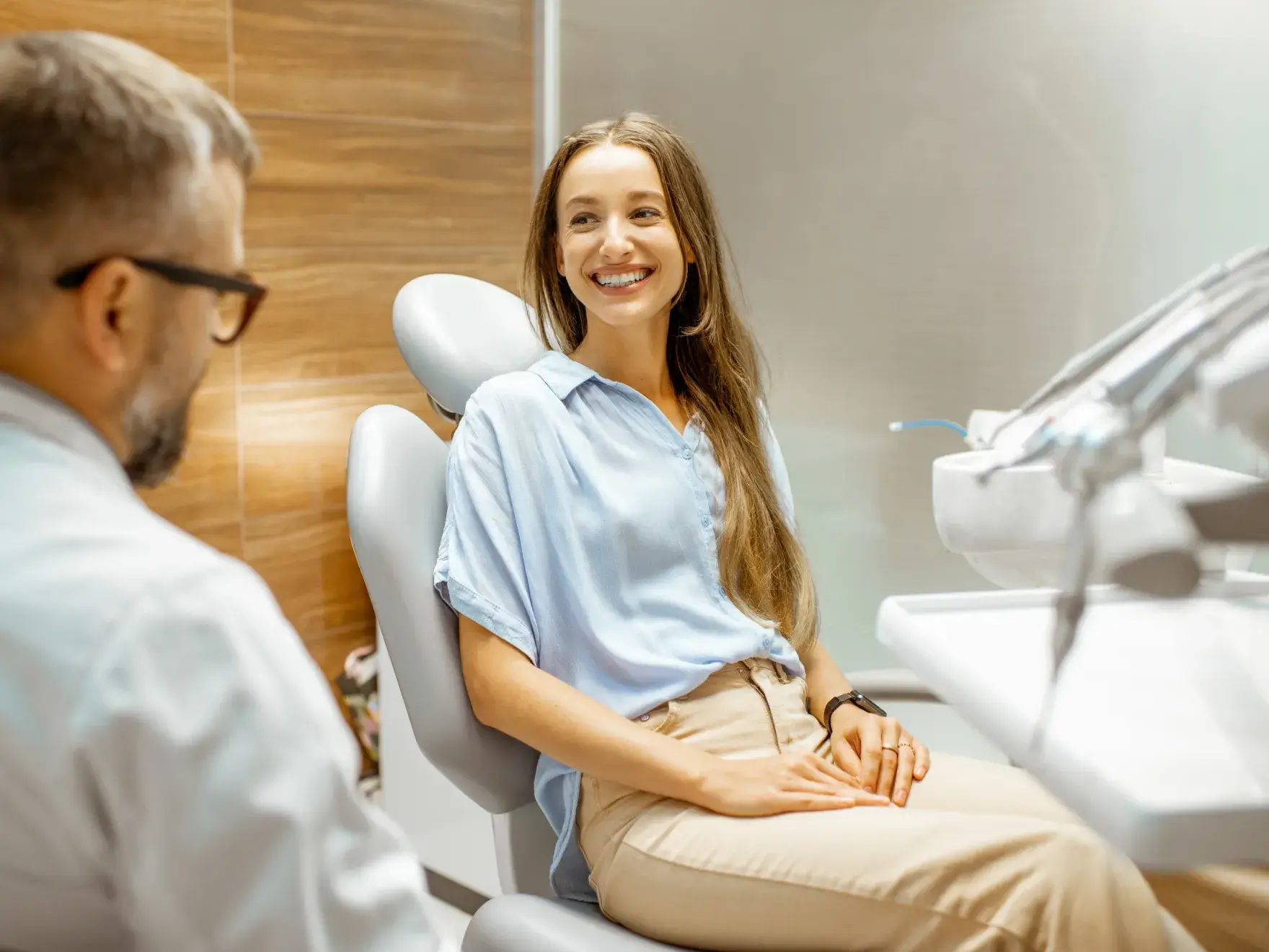 Smiling woman wearing braces sitting in a dental chair talking with a male dentist in a modern clinic.