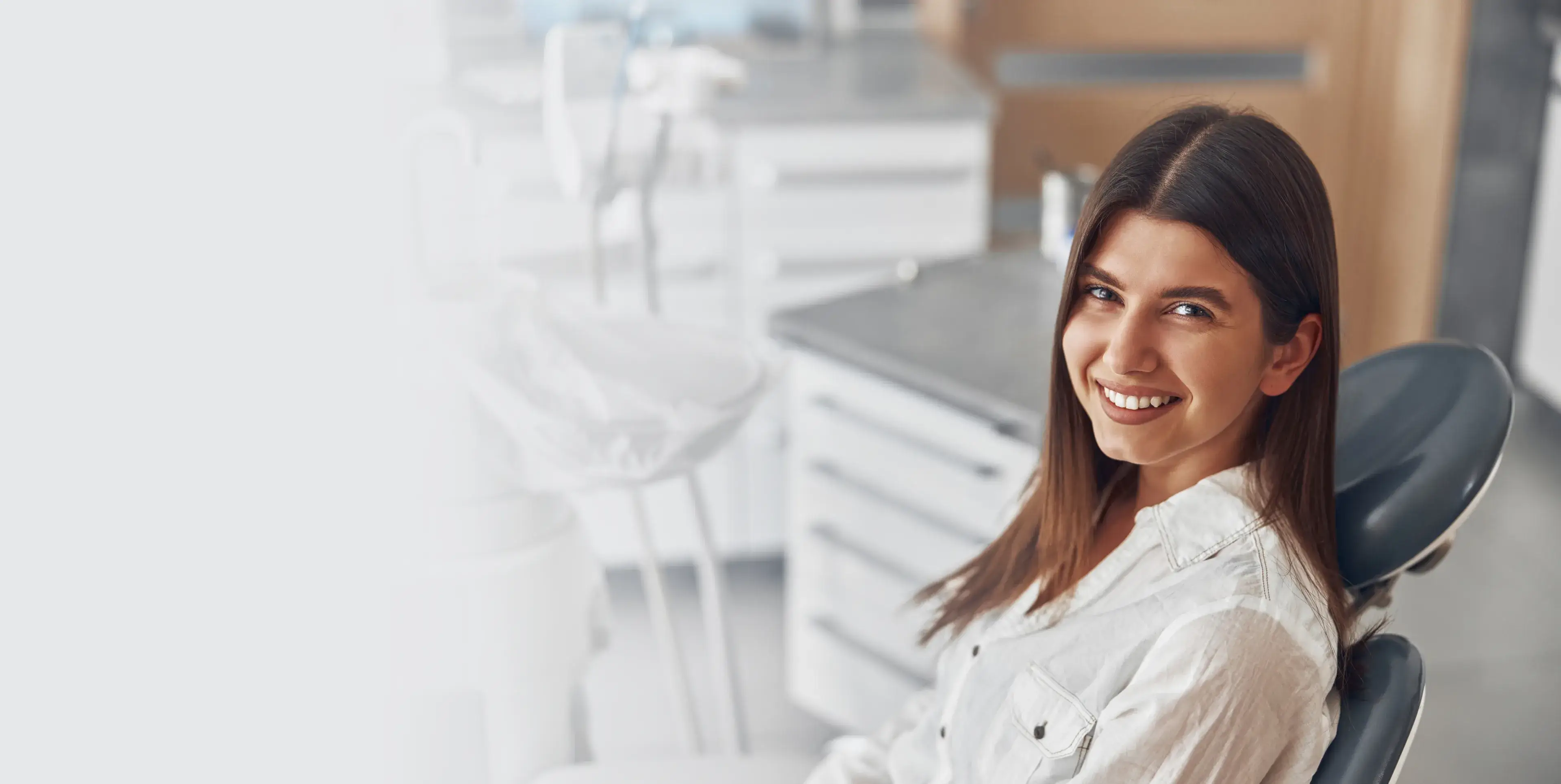 Smiling young woman sitting in a dental chair in a bright dental office.