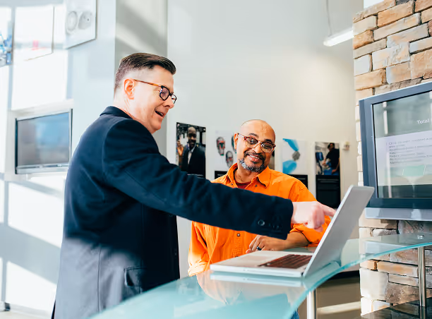 Deux hommes regardant un ordinateur portable posé sur un comptoir dans un espace de travail lumineux.