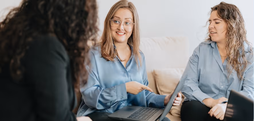 Trois femmes assises discutent autour d'un ordinateur portable dans un cadre informel.