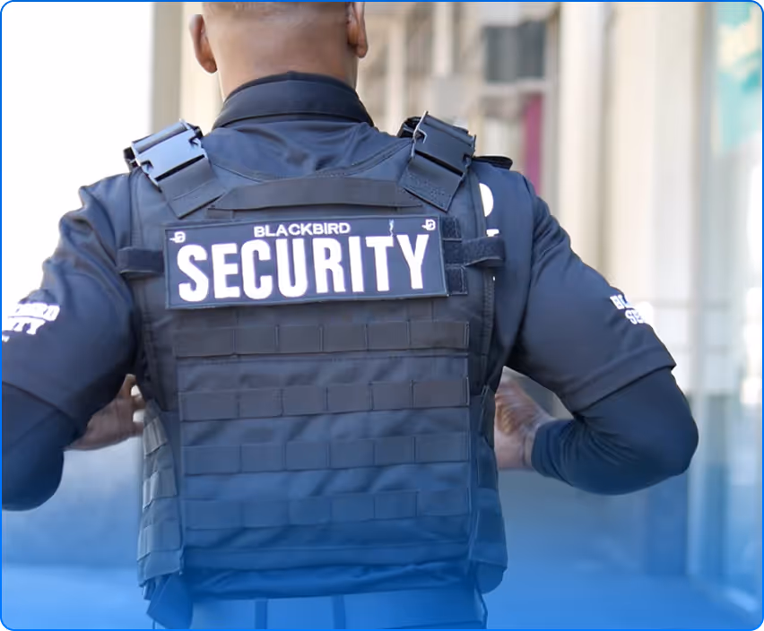 Back view of a security guard wearing a black tactical vest with a patch labeled 'BLACKBIRD SECURITY'.