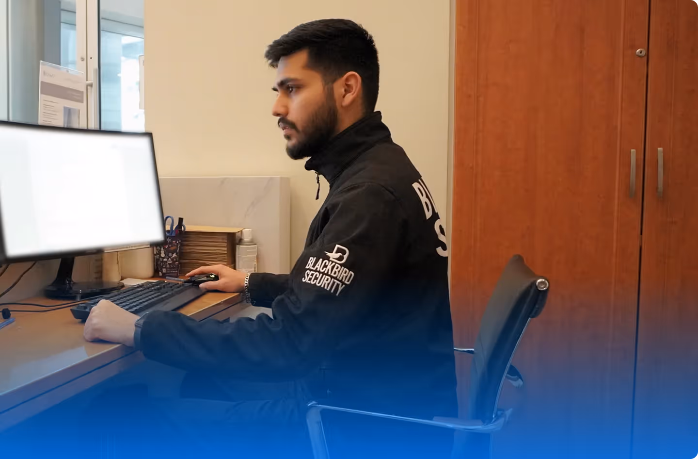 Man in Blackbird Security jacket working on a computer at a desk in an office.