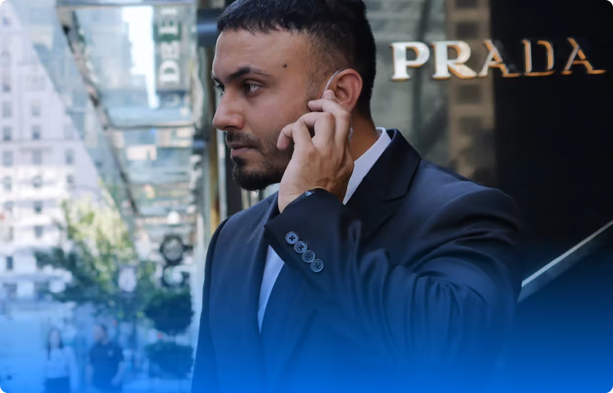 Man wearing a suit adjusting an earpiece outside a Prada store in a city setting.