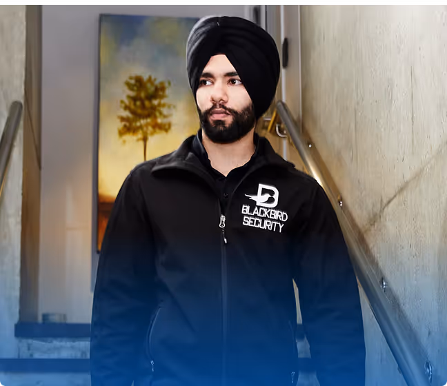 Man wearing a black turban and a Blackbird Security jacket standing on stairs next to a handrail.