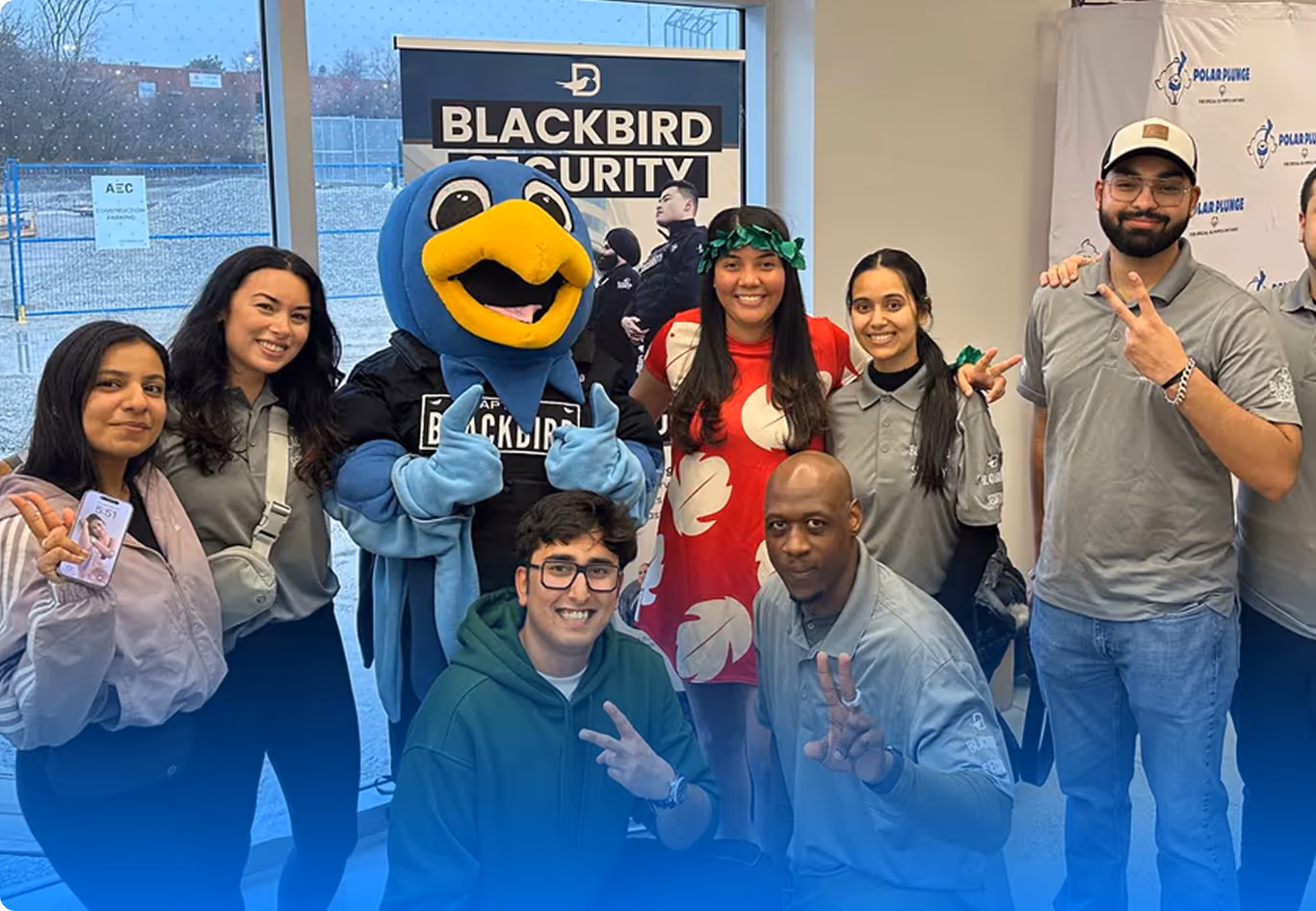 Group of smiling people posing indoors with a person dressed in a blue bird mascot costume and a Blackbird Security banner in the background.