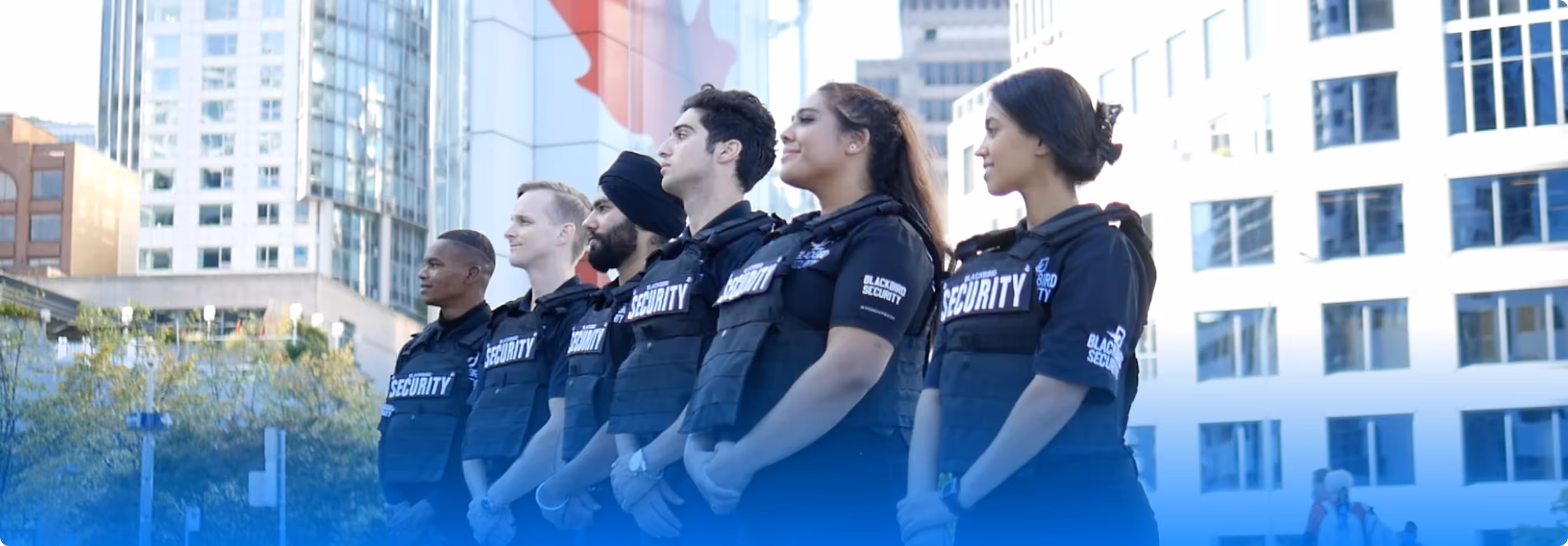 Six diverse security guards standing in a row outside in front of urban buildings.