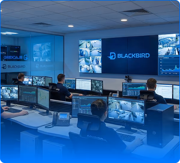 Control room with multiple monitors displaying surveillance footage and the Blackbird logo on a large screen, staffed by individuals monitoring security.