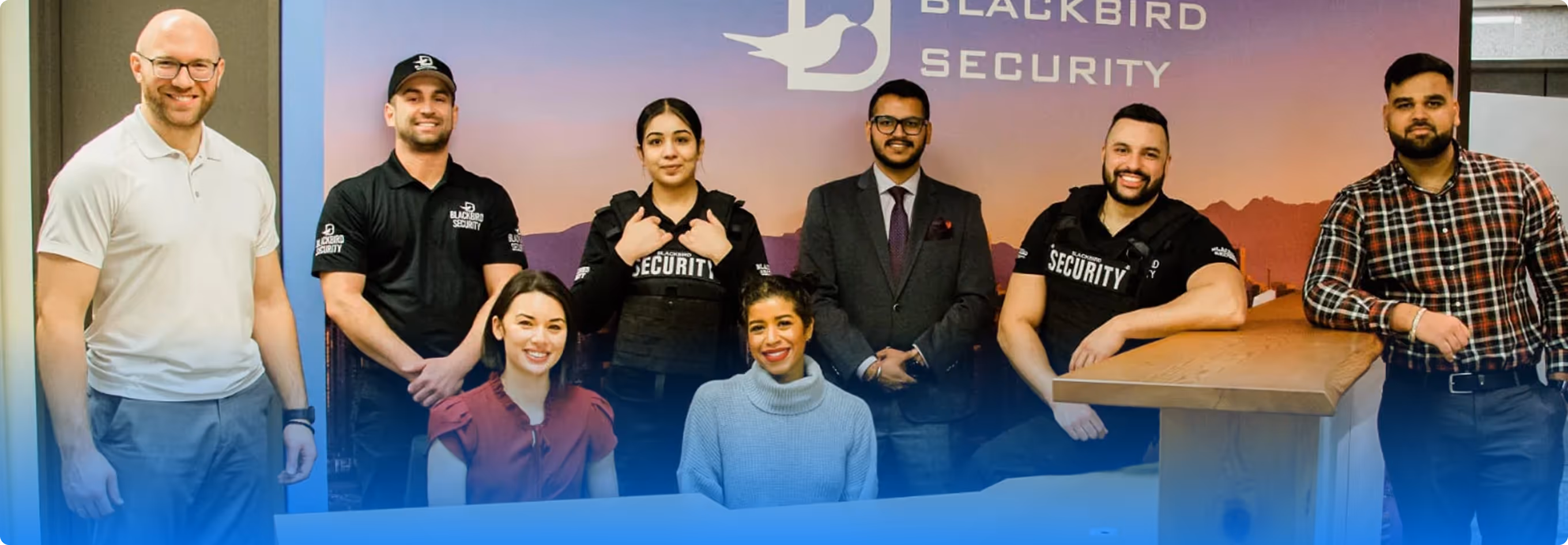 Group of eight diverse Blackbird Security team members posing in front of a company sign.