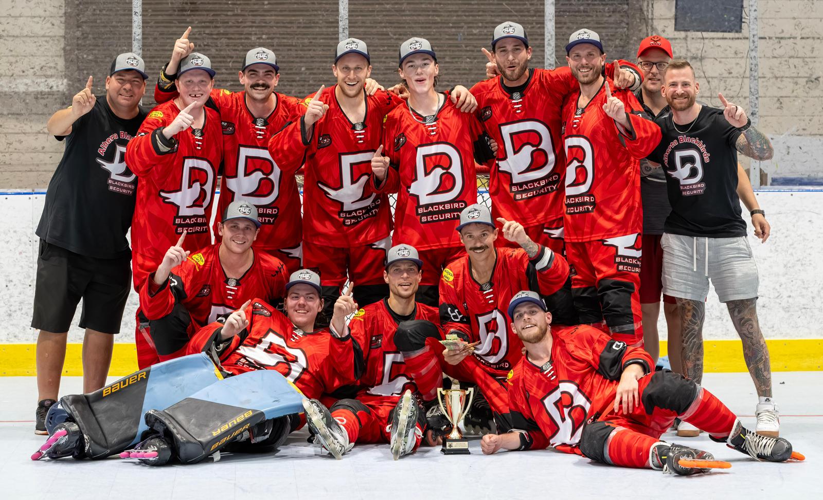 A victorious roller hockey team in red jerseys and grey hats posing with a trophy on the rink, showing number one gestures.