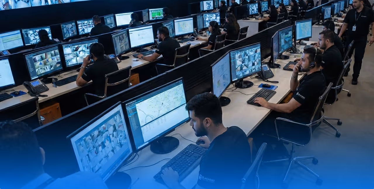 A control room with multiple operators monitoring several computer screens displaying surveillance footage and maps.