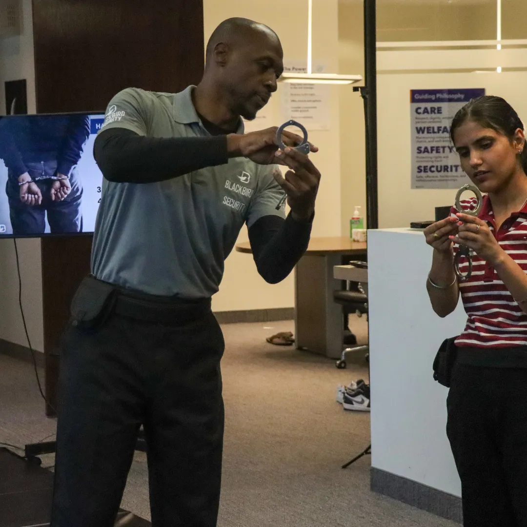Two security officers practice locking handcuffs indoors in a training room.