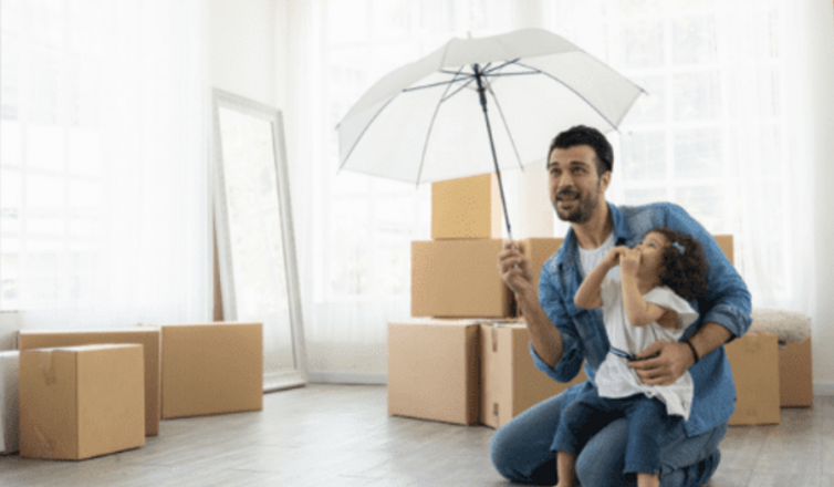 Father and daughter holding umbrella while moving into new home with cardboard boxes