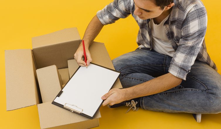 Man writing complete checklist on clipboard surrounded by moving boxes