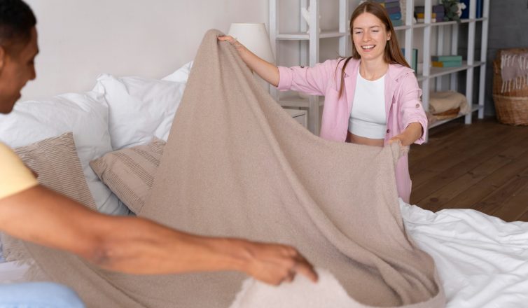 "Two women folding blanket to pack bedding for moving day in bedroom