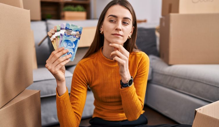 Woman holding cash considering how much to tip movers surrounded by moving boxes
