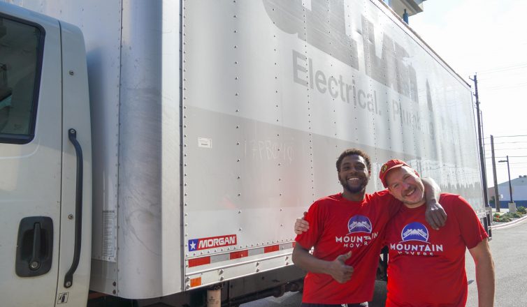 Two professional movers in red uniforms standing by moving truck ready to hire movers