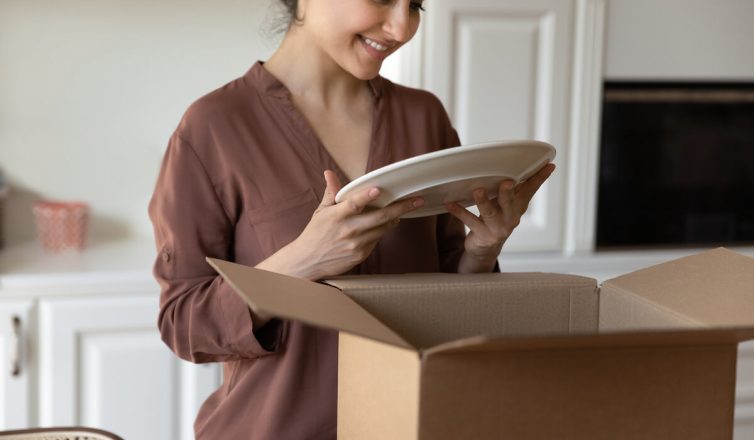 Woman carefully wrapping plates to pack dishes safely in moving box