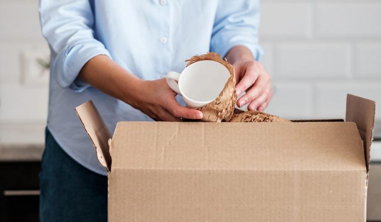 Moving mugs and dishes with crinkle paper padding in cardboard boxes for safe kitchen item relocation