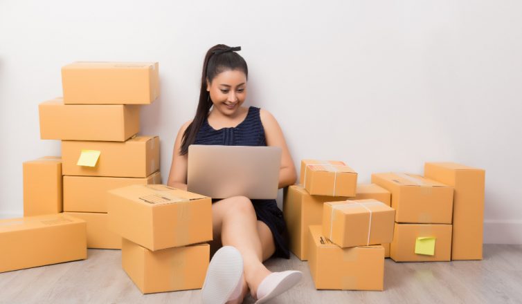 Woman with laptop organizing belongings in cardboard boxes during move