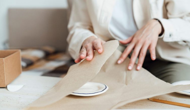 Person wrapping china dishes with packing paper for safe moving