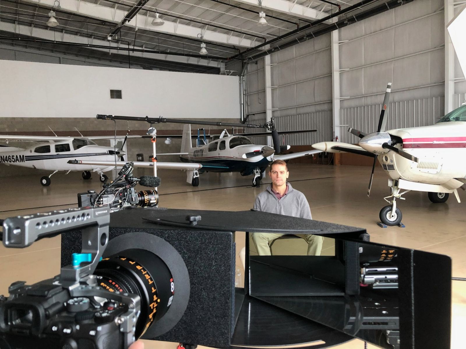 Behind-the-scenes view of a film production set inside an airplane hangar, featuring a crew member reviewing notes next to a professional camera rig and lighting equipment