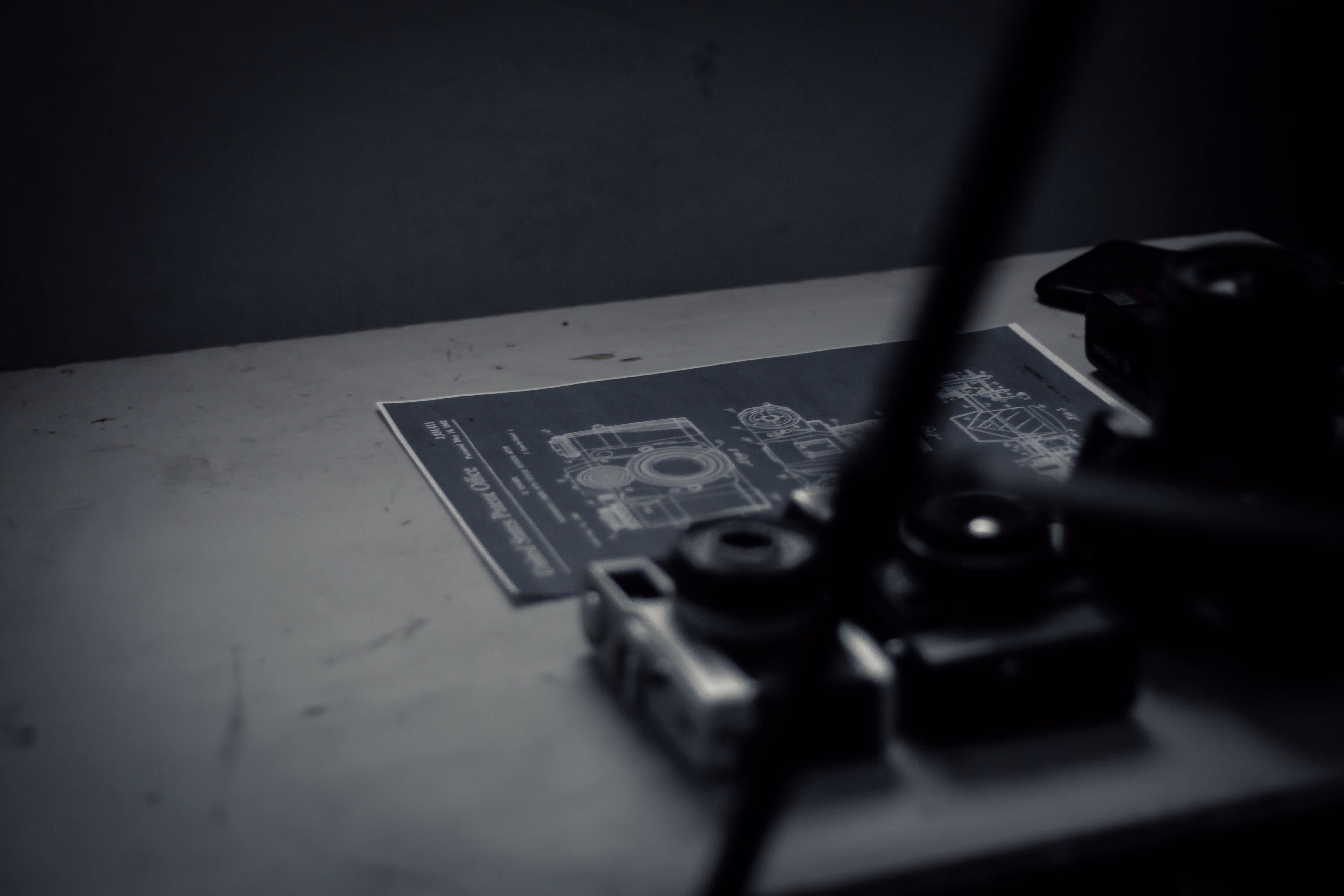 Black and white image of a camera blueprint on a table with vintage cameras placed nearby.