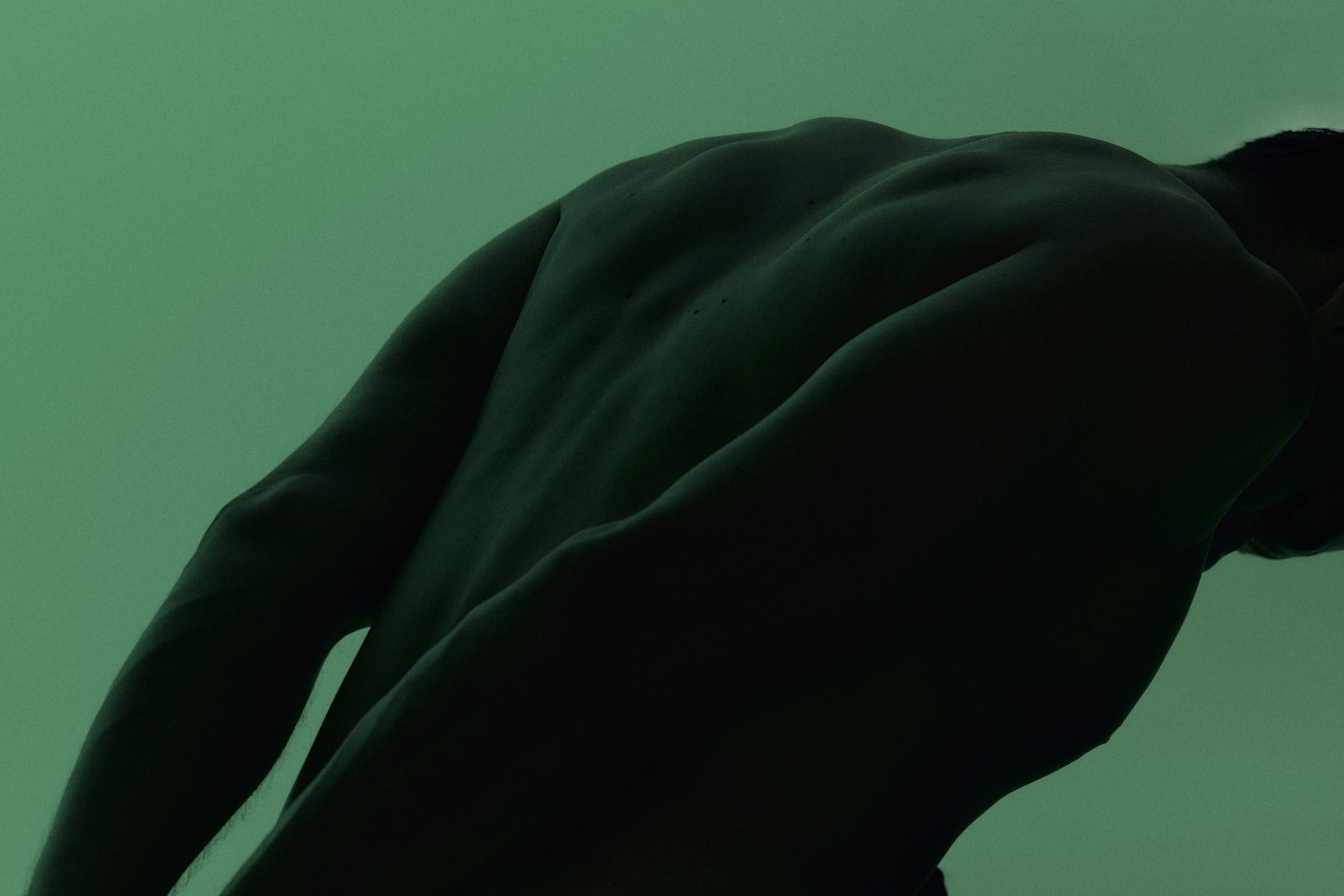 Close-up side view of a muscular man's bare back and arms against a green background.