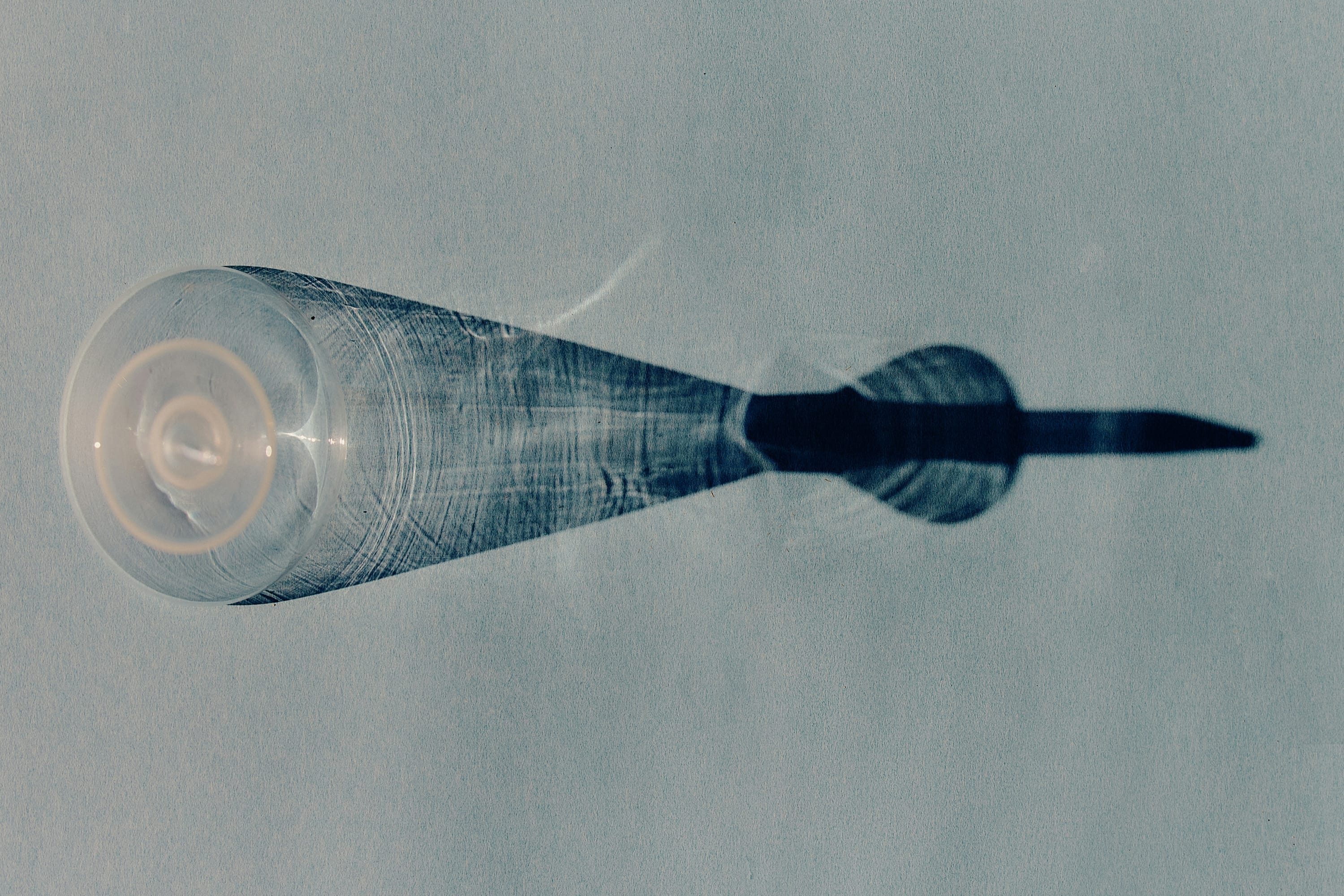 Top-down view of a clear glass turned upside down casting an elongated shadow on a textured surface.