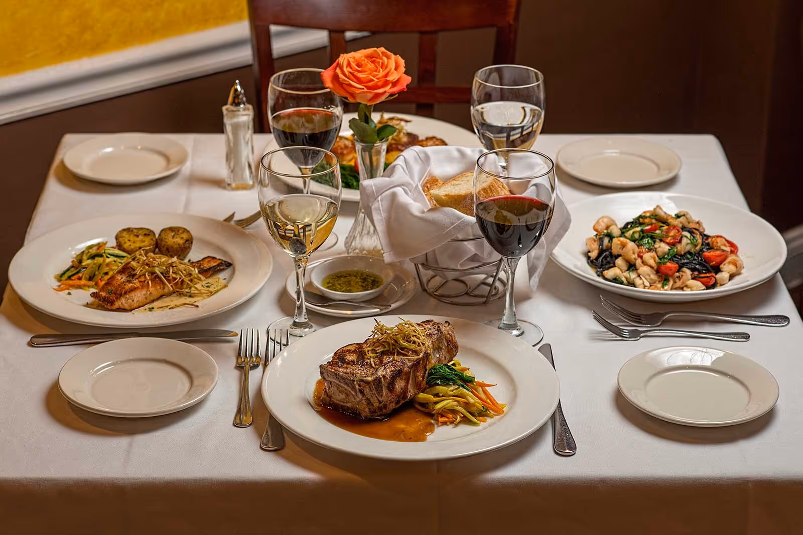 Multiple entrees with focs on steak and glass of red wine